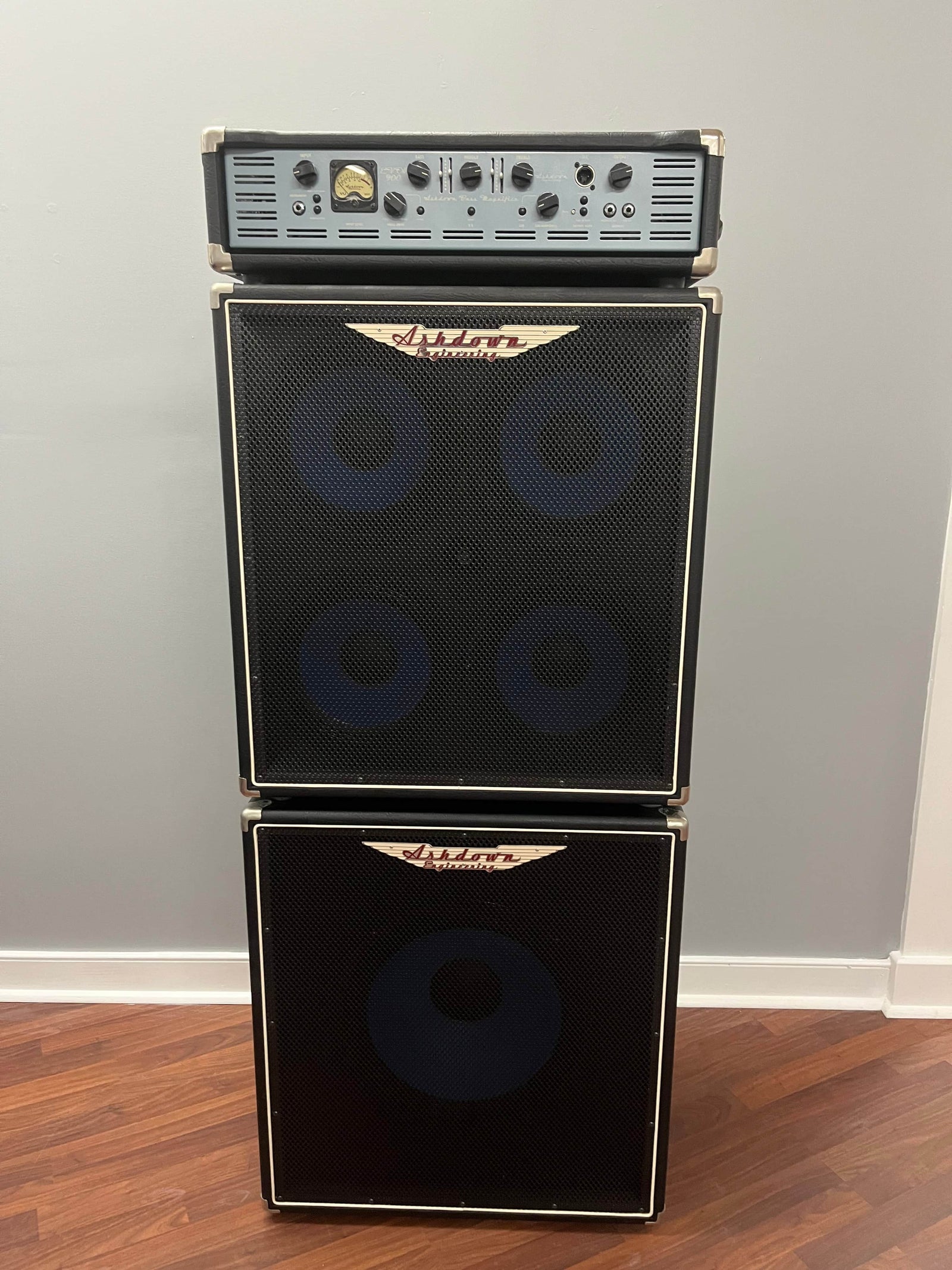 An Ashdown UK Built ABM Bass Rig Full Stack, with an EVO II 900 Head and 410T & 115-500 cabinets in flight cases, stands on a wooden floor against a light-colored wall.
