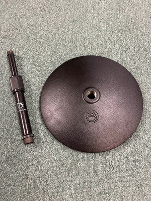 An Atlas Sound DMS7E Mic Stand Base with Extension Rod, featuring a round base with central hole and engraved logos, is placed on a textured gray carpet.