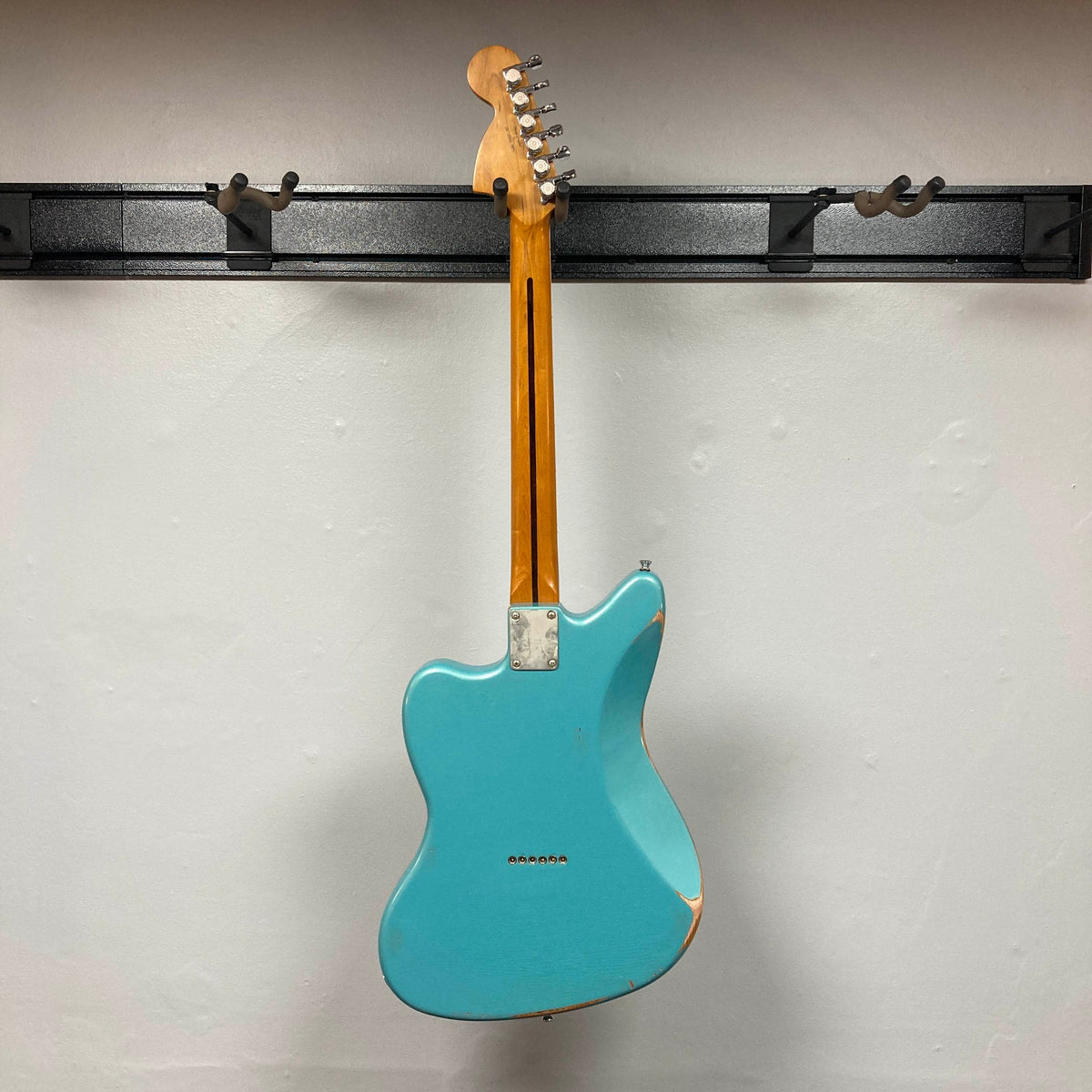 Back view of a distressed Big River Jazzcaster Custom Relic Pelham Blue Used electric guitar hanging on a wall-mounted guitar rack.