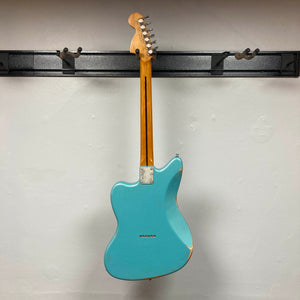 Back view of a distressed Big River Jazzcaster Custom Relic Pelham Blue Used electric guitar hanging on a wall-mounted guitar rack.