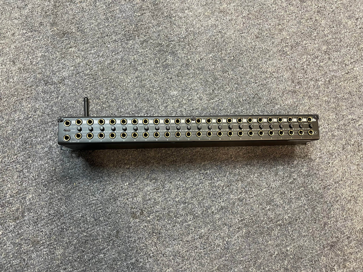 A Black Lion Audio PBR TRS-BT 46-Point Gold-Plated TRS Patchbay with Bluetooth sits on a gray carpeted surface, displaying two rows of circular jacks and a lever on the left side.