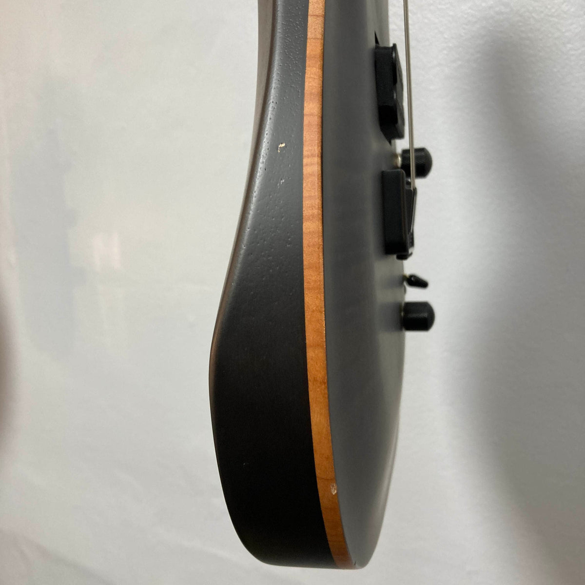Side view of the Chapman ML1 Pro Modern Lunar electric guitar by Chapman, showcasing its natural wood edge, 24-fret neck, dual humbucker pickups, and black control knobs—all set against a light-colored wall.