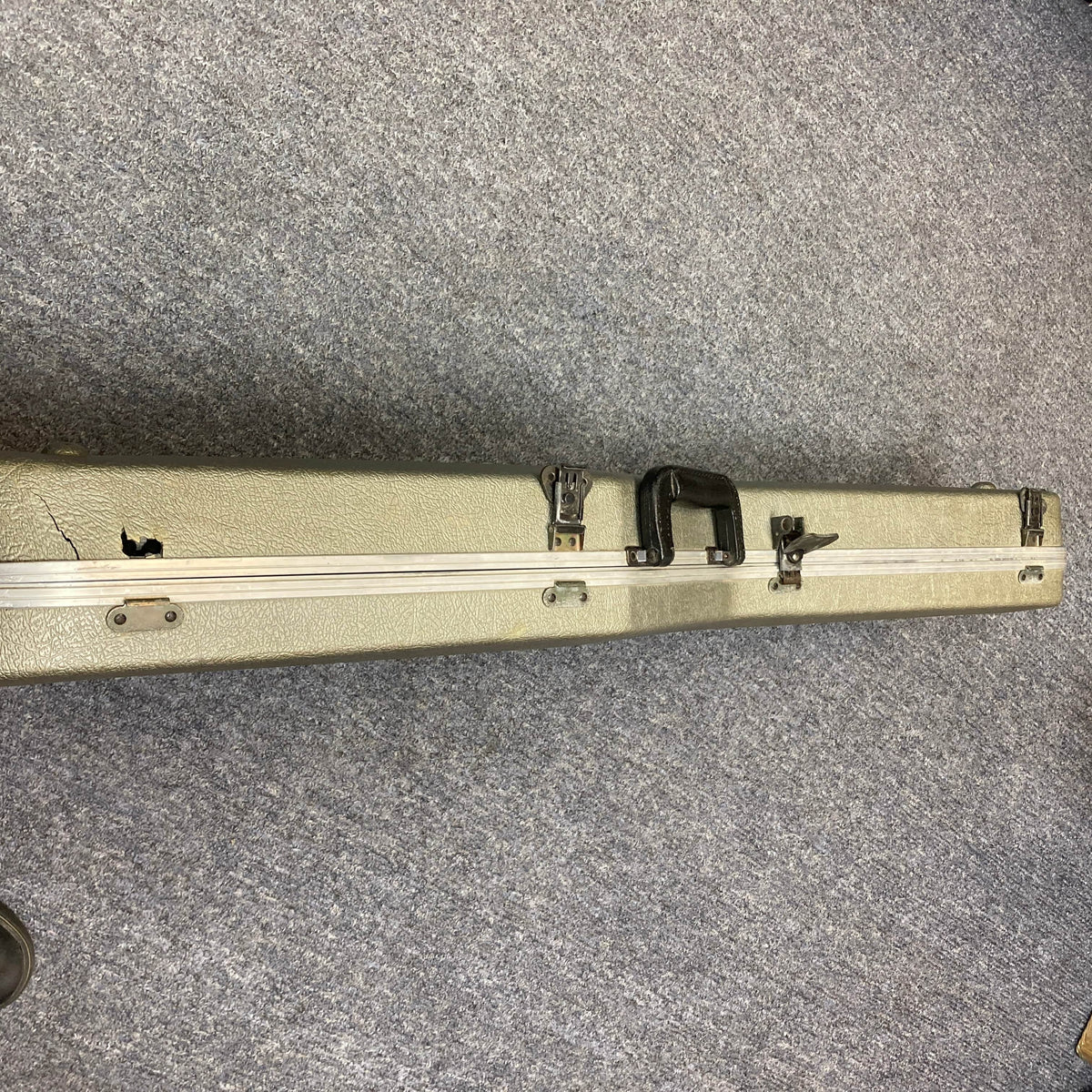 A Charvel Model 4 HSS Red with original hard case showing visible damage and a crack on the left side, resting on a gray carpet—ideal for safely storing your vintage Charvel guitar.