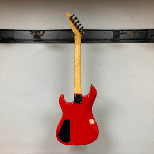 A Charvel Model 4 HSS Red w/OHSC Consign electric guitar by Charvel hangs on a black wall mount, photographed from the back to showcase its neck and body.