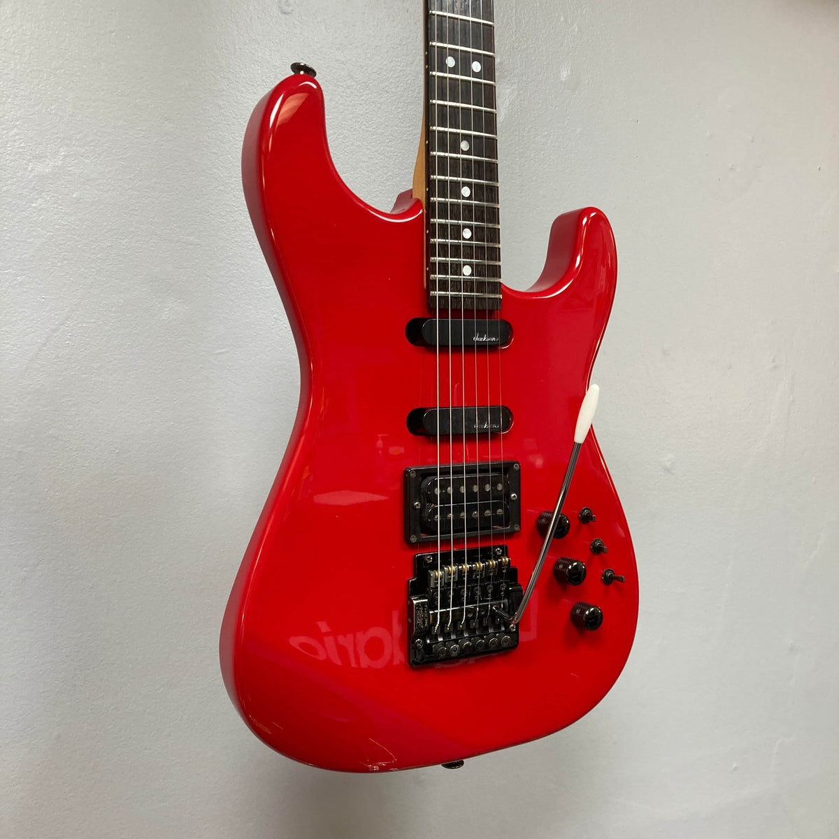A Charvel Model 4 HSS Red w/OHSC Consign electric guitar with black hardware, three pickups, and multiple control knobs is shown against a light gray wall.