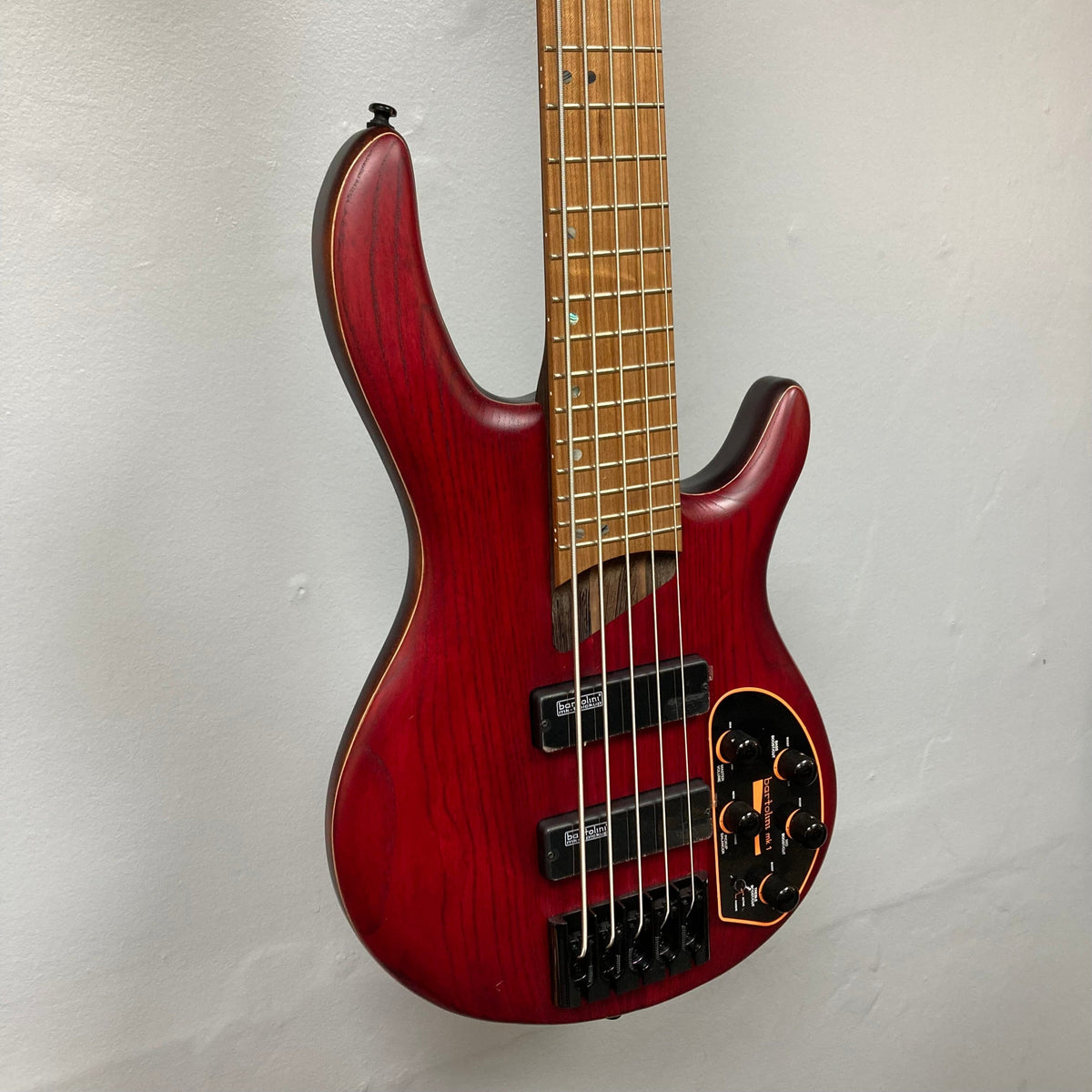 Cort B5 Artisan Element Open Pore Burgundy Red Bass Guitar mounted on a wall, featuring a roasted maple fretboard and Bartolini MK-1 pickups.