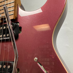 Close-up of the Cort FW-G300 PRO Vivid Burgundy electric guitar body, featuring its pickups, strings, whammy bar, and part of the neck against a plain light-colored wall.