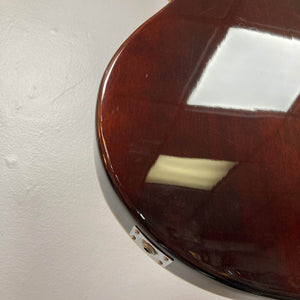 Close-up of the bottom edge of a dark, glossy Crafter SA-BUB Acoustic Electric Guitar Used Consign by Crafter, reflecting ceiling lights; a metal input jack is visible at the base for plugged-in use.