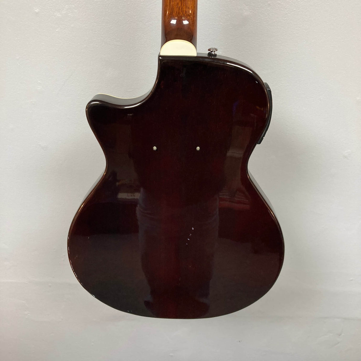 The back of a used Crafter SA-BUB Acoustic Electric Guitar is shown against a white wall, highlighting its dark brown finish, single cutaway design, and two visible dots—perfect for your next plugged in performance.