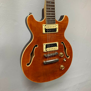 A Dean Boca Trans Amber Burst 12 String guitar by Dean, featuring a glossy amber finish and included gigbag, is mounted on a light gray wall.