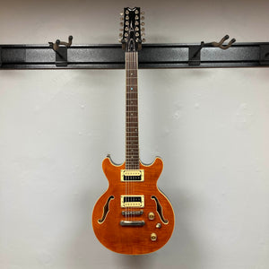 A Dean Boca Trans Amber Burst 12-string electric guitar by Dean, with gigbag, hangs on a wall-mounted rack.