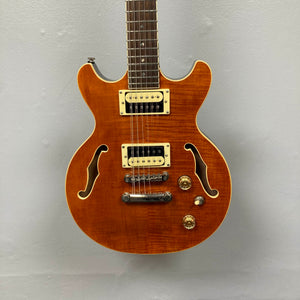 The Dean Boca Trans Amber Burst 12 String w/Gigbag by Dean is shown with a striking amber burst finish, twelve strings, two pickups, four control knobs, and two f-holes against a plain light gray background.