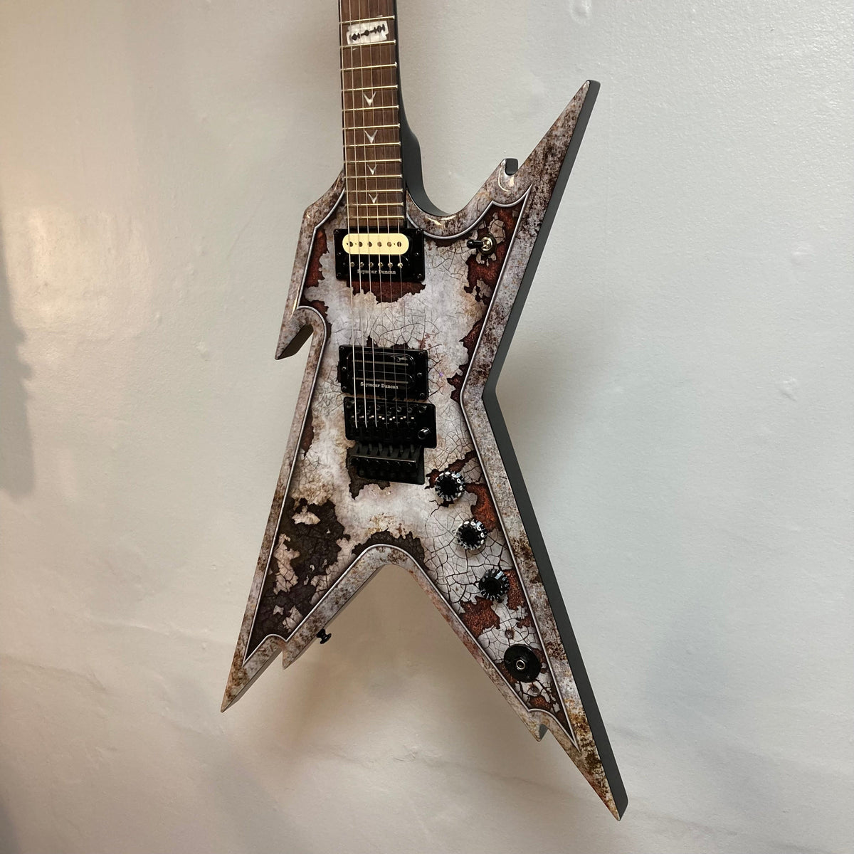 Dean Razorback Rust electric guitar with rusted design hanging on a wall, highlighting minor blemishes and unique custom graphic. Comes with a protective case.