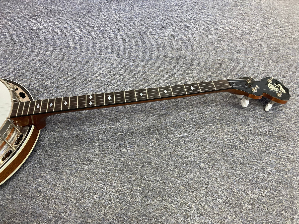 Deering Deluxe 4-String Banjo lying on the floor, showcasing its strings and craftsmanship.