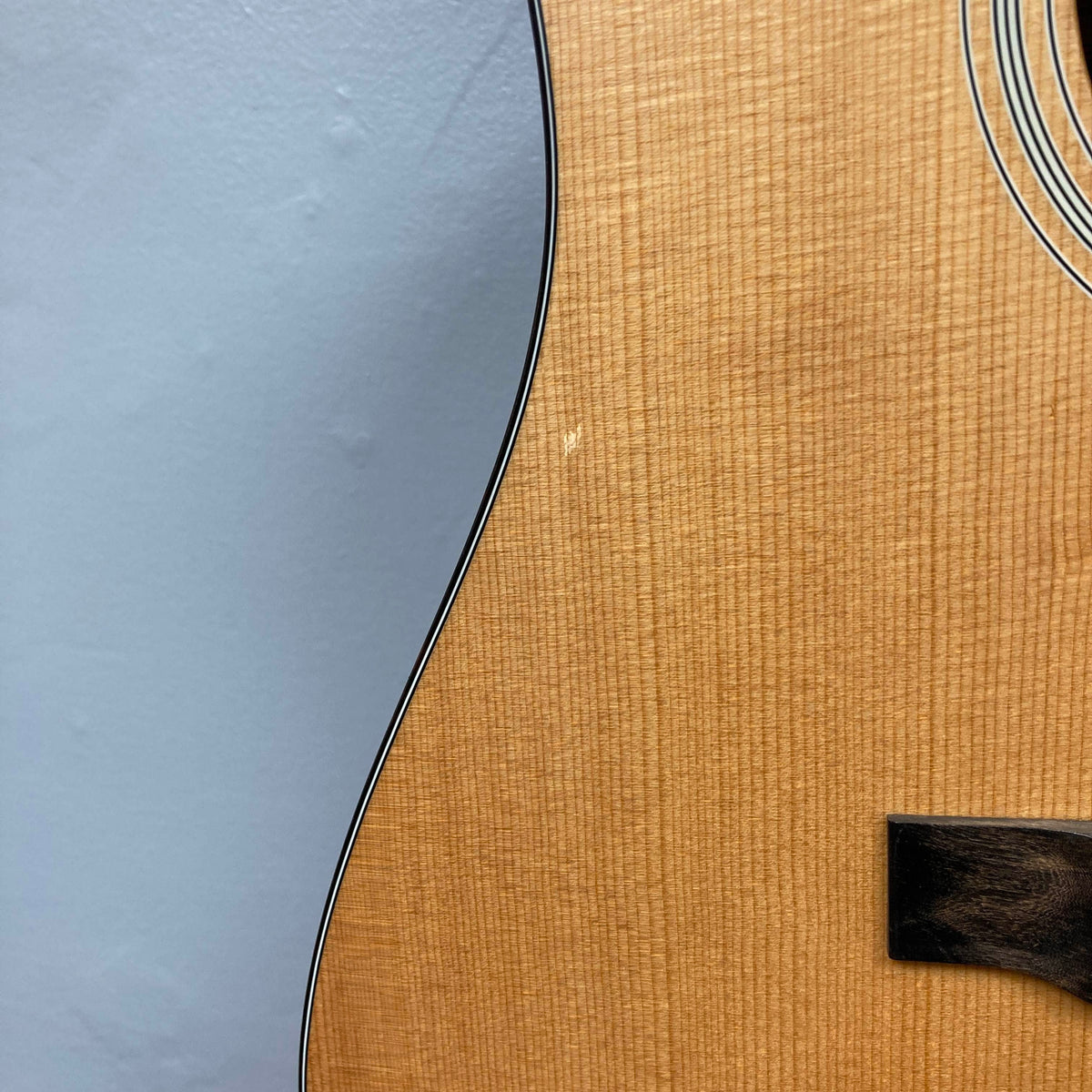 Close-up of the solid Sitka spruce top of an Eastman E1D Dreadnought Natural w/Gigbag Used acoustic guitar, showing a small scratch near the edge of the soundboard.