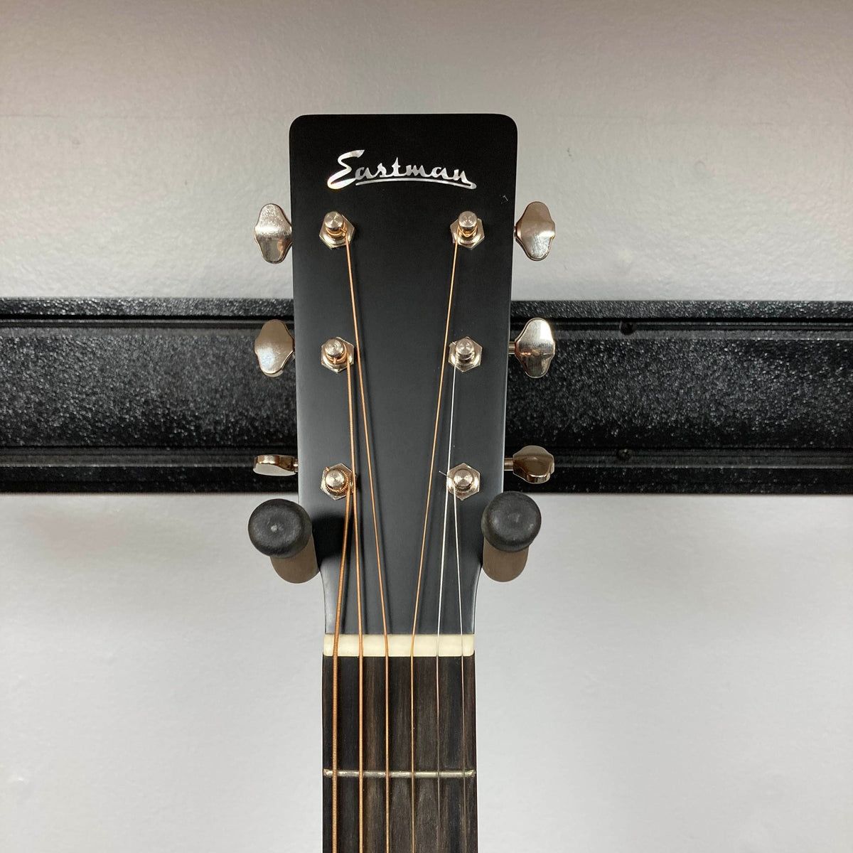 Eastman E1D Dreadnought Natural w/Gigbag Used headstock with silver tuning pegs and six strings, mounted on a wall bracket.