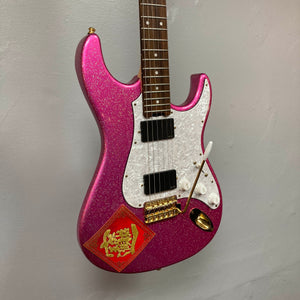 Edwards ESP E-SN-185-TO Takayoshi Ohmura Twinkle Pink electric guitar, featuring dual humbuckers, a sparkling pink glitter finish, white pickguard, gold hardware, and a red decorative sticker in the lower corner, photographed against a plain gray wall.