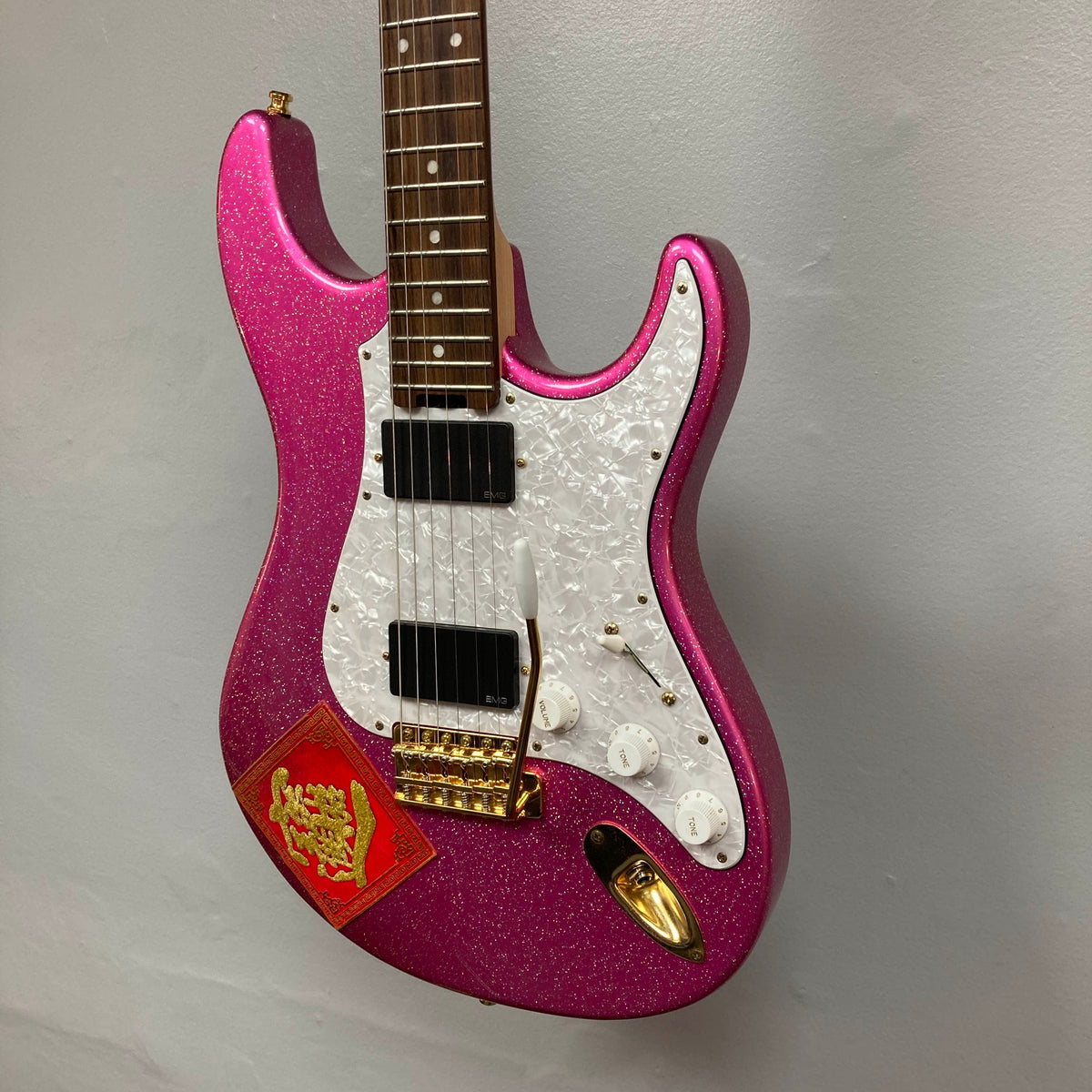 An Edwards ESP E-SN-185-TO Takayoshi Ohmura electric guitar in Twinkle Pink, featuring dual humbucker pickups, a white pickguard, gold hardware, and a red envelope with a gold Chinese character attached to the body.