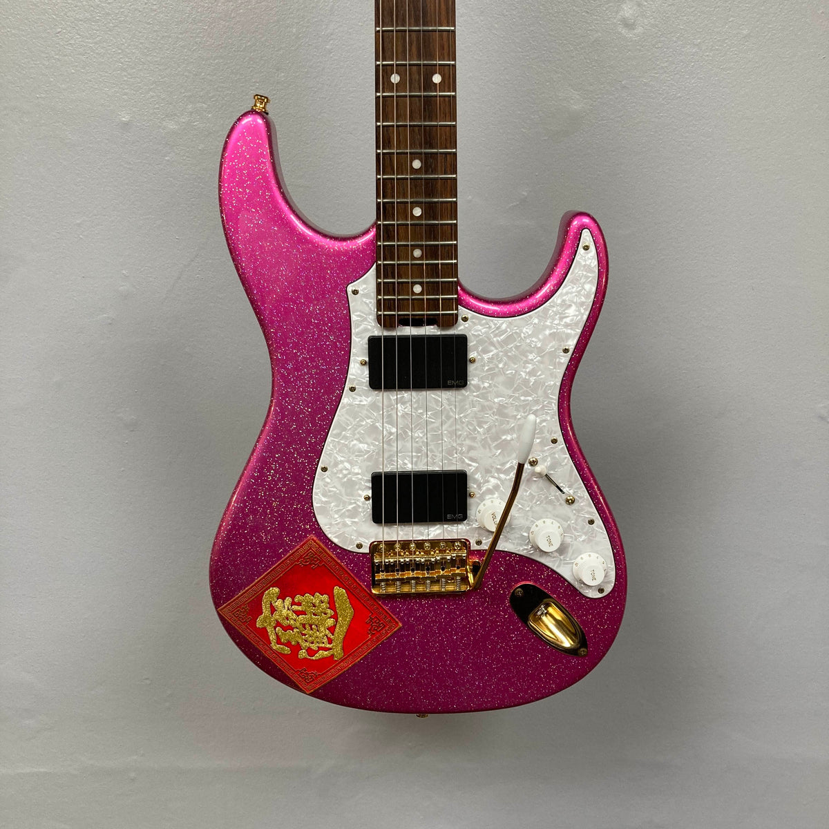 An Edwards ESP E-SN-185-TO Takayoshi Ohmura electric guitar in Twinkle Pink, featuring dual humbuckers, a white pickguard, gold hardware, and a red sticker with Chinese characters and a gold dragon on the lower body, displayed against a plain gray background.
