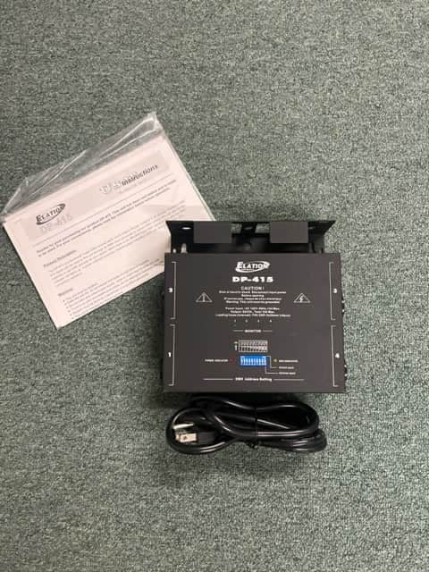 A black Elation Professional DP-415 4-Channel Dimmer/Power Pack is shown on a gray carpet with a power cord and manual, ideal for DMX-compatible stage lighting control.