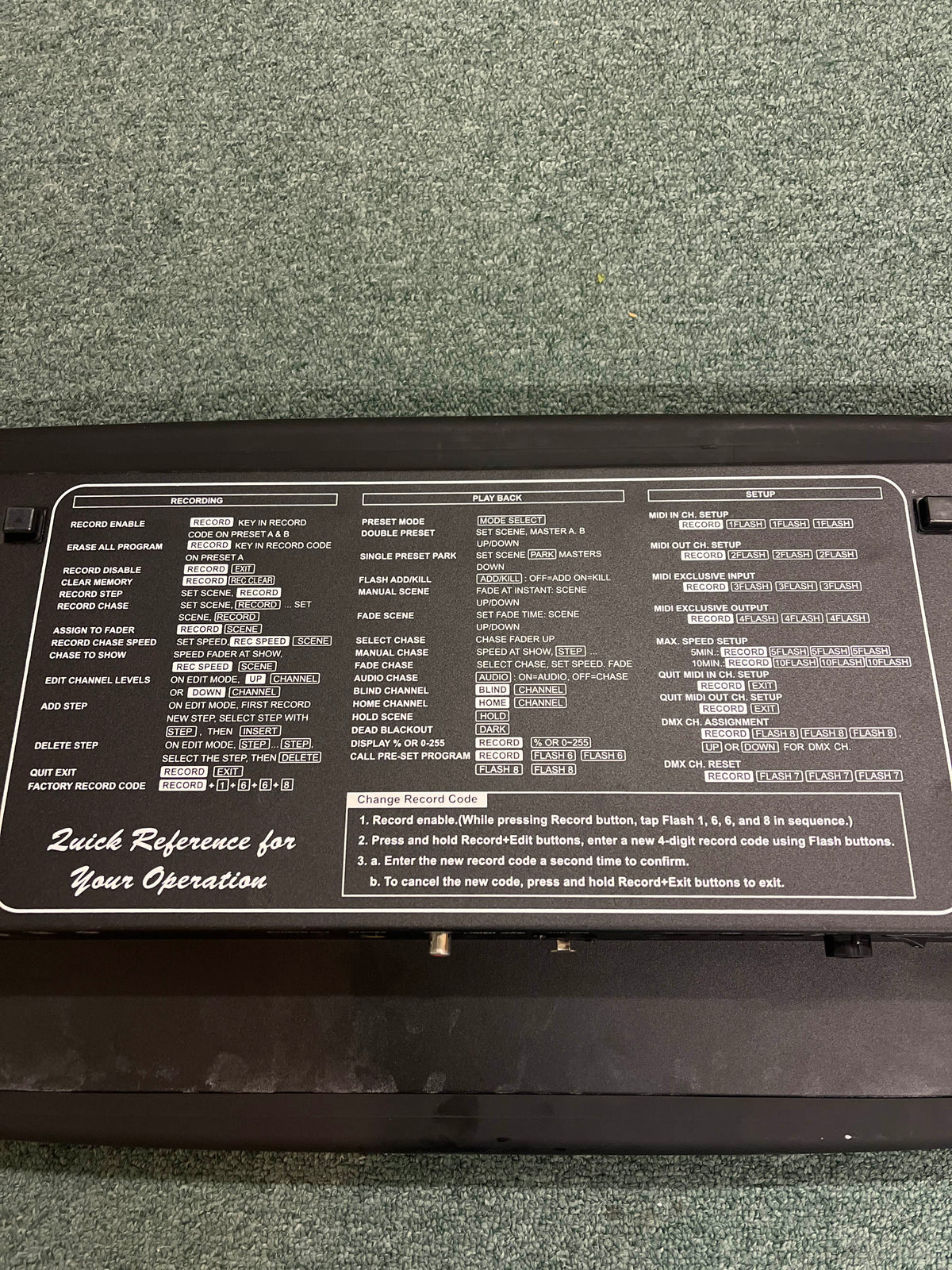 The Elation Scene Setter 24-Channel DMX Dimmer Console features a black control panel with white text and button labels, showing programming and playback instructions. It is placed on green carpet, providing efficient lighting control for any setup.