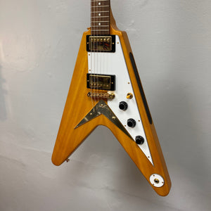 Epiphone 1958 Korina Flying V guitar with visible knobs, switches, and strings, displayed on a wall.