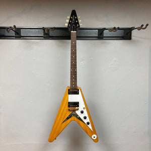 Epiphone 1958 Korina Flying V guitar on a wall hook, showcasing its solid Korina body, gold hardware, and included hardshell case.