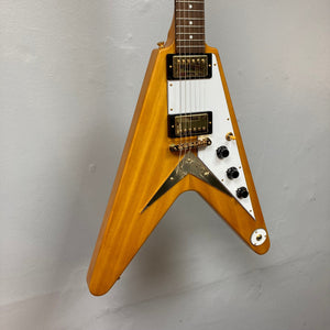 Epiphone 1958 Korina Flying V w/Case displayed on a wall, showcasing its vintage design, Korina body and neck, and gold hardware.