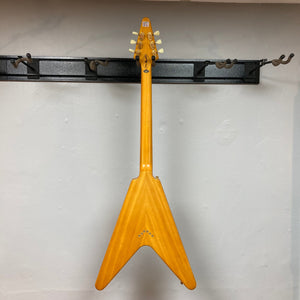 Epiphone 1958 Korina Flying V guitar on a stand, showcasing its vintage-inspired design and premium features, including a solid Korina body and gold hardware.