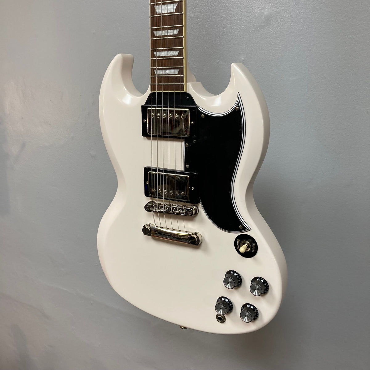 Epiphone 1961 Les Paul SG Standard Aged Classic White electric guitar, featuring distinctive body contours and vintage-style hardware, displayed on a wall.