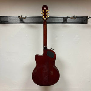 An Epiphone Chet Atkins SST Studio Natural semi-hollow electric guitar, with gold tuners and a black electronics cover, hangs on a wall rack; its feedback-resistant design stands out against the white wall.