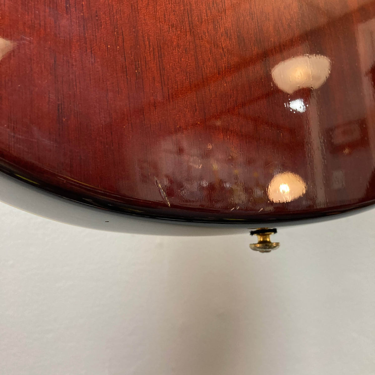 A close-up of the bottom edge of an Epiphone Chet Atkins SST Studio Natural Korea guitar, showing a small scratch and strap button. Reflections highlight this used consignment acoustic electric’s surface. Hard case included.