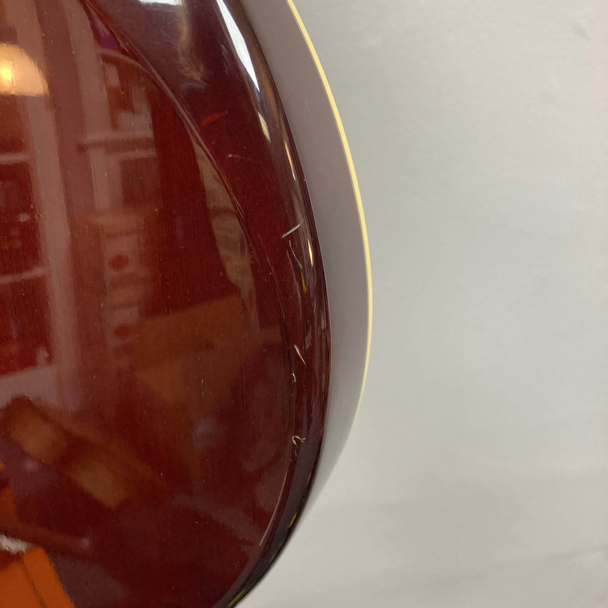 Close-up of the back of an Epiphone Chet Atkins SST Studio Natural (Korea, used) showing light scratches on the glossy reddish-brown finish near the edge, set against a pale gray background.