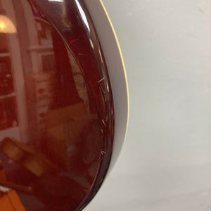 Close-up of the back of an Epiphone Chet Atkins SST Studio Natural (Korea, used) showing light scratches on the glossy reddish-brown finish near the edge, set against a pale gray background.