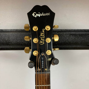 Close-up of an Epiphone Chet Atkins SST Studio Natural guitar headstock with gold tuning pegs, "Gibson" truss rod cover, and a gold signature on black, evoking its feedback-resistant acoustic-electric design. Brand: Epiphone.