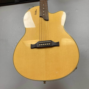 A close-up of an Epiphone Chet Atkins SST Studio Natural acoustic-electric guitar, featuring a cutaway design and six strings, hanging against a gray wall. Brand: Epiphone. Includes hard case. Used consignment, made in Korea.
