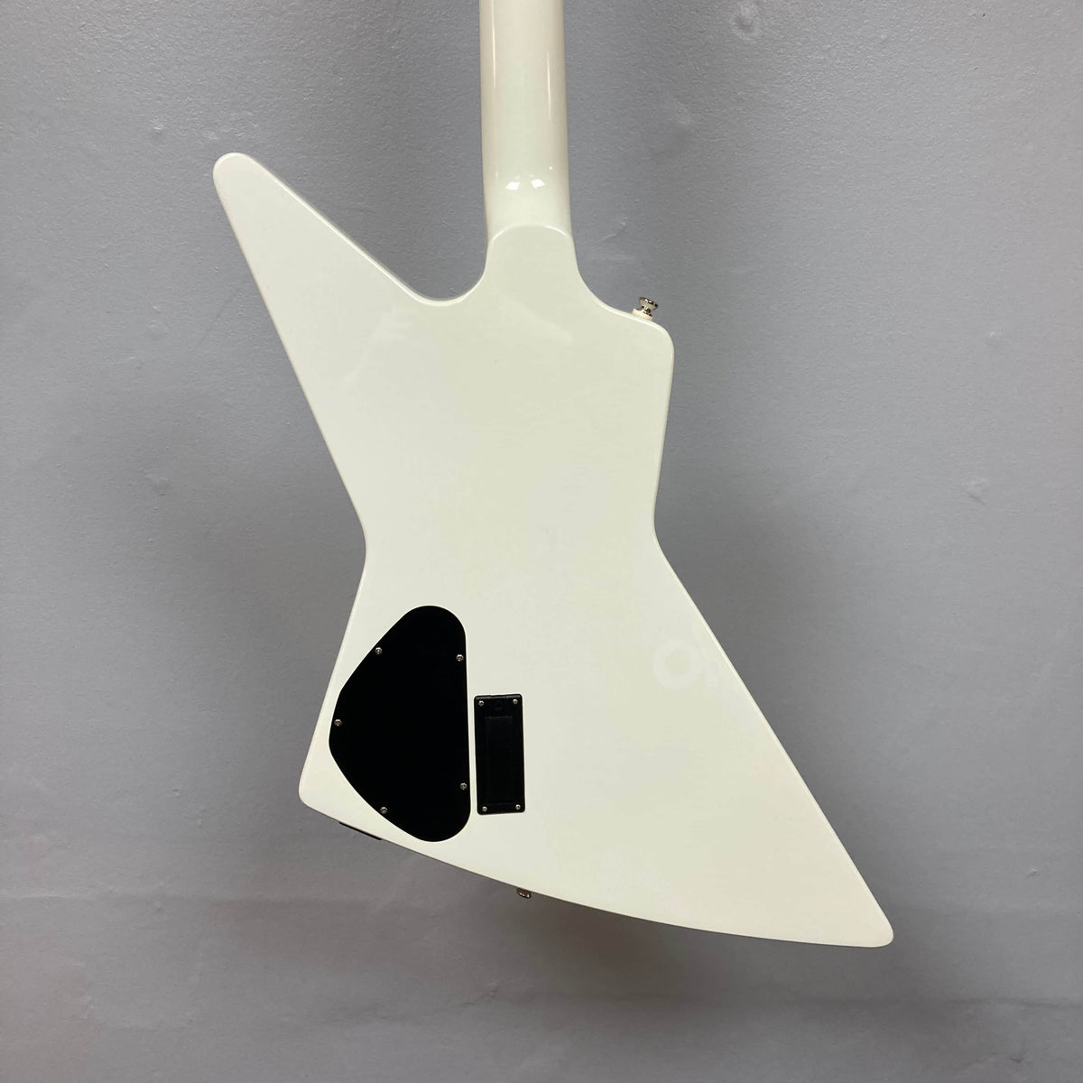 Back view of the Epiphone Explorer 80s EMG Classic White w/Gigbag by Epiphone, showing its angular body, black cover plate, and rectangular compartment against a plain gray background.