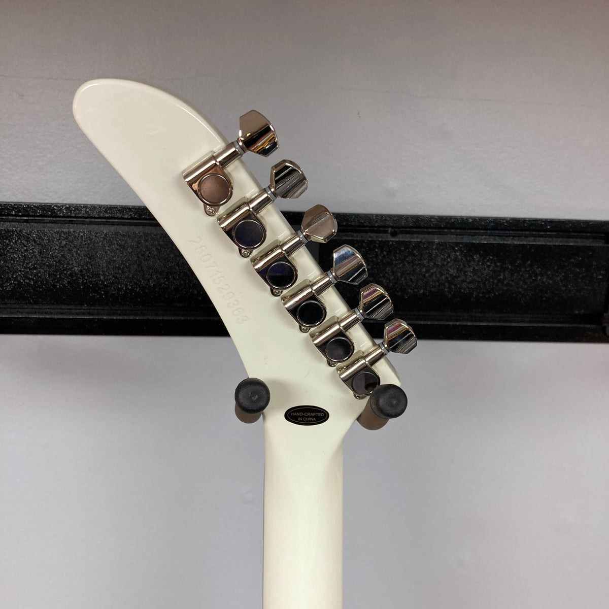 Back view of the Epiphone Explorer 80s EMG Classic White electric guitar headstock with six tuners, mahogany neck, on a black wall hanger against a light wall. Includes gigbag. Brand: Epiphone.