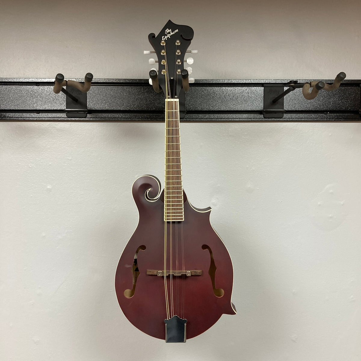 Epiphone F-5 Studio Mandolin in Wine Red Satin hanging on a display wall, showcasing its vintage F-style design and craftsmanship.