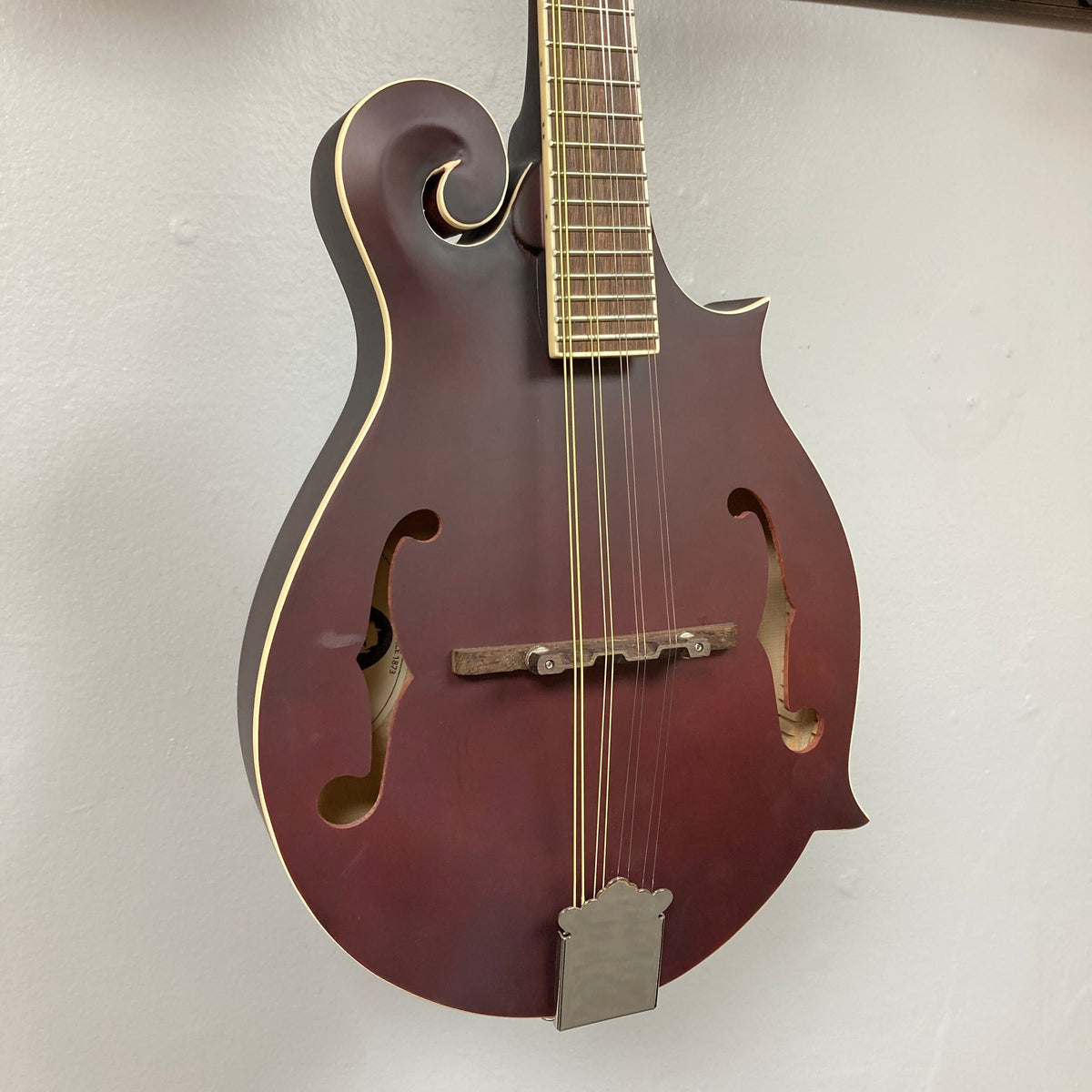 Epiphone F-5 Studio Mandolin - Wine Red Satin displayed on a wall, highlighting its F-style body with strings and neck details.