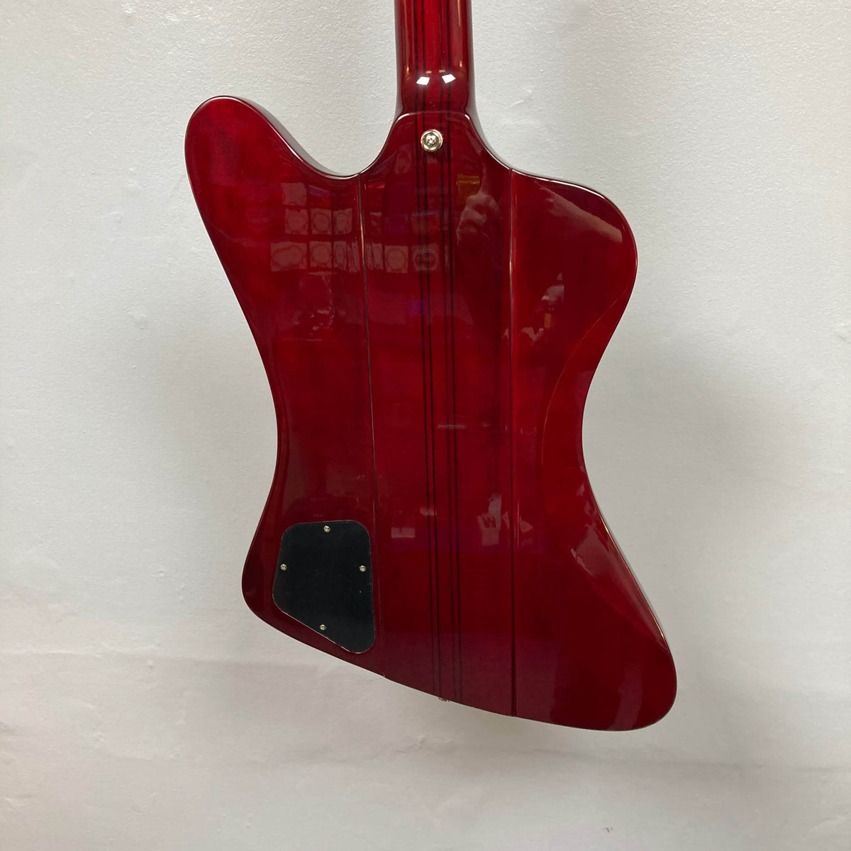 The Epiphone Firebird Wine Red w/Gigbag is displayed from the back, showing its glossy red body, black rectangular backplate, and bolt-on neck against a white wall.
