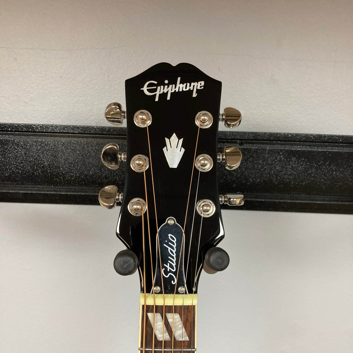 Close-up of the Epiphone Hummingbird Studio Antique Natural headstock, showing six tuning pegs, the Epiphone logo, emblem, and a "Studio" truss rod cover—part of this model with a solid spruce top. Comes with gigbag.