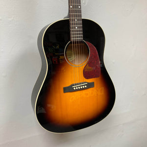 An Epiphone J-45 Studio Vintage Sunburst acoustic guitar with a tortoiseshell pickguard and solid spruce top hangs on a white wall. This six-string guitar by Epiphone features a glossy finish and comes with a gigbag.