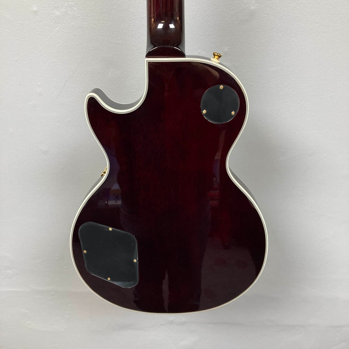 Back of the Epiphone Jerry Cantrell Wino Les Paul Custom in Wine Red with cream binding, two access panels, and part of the neck shown against a light background; includes custom Epiphone hardshell case.