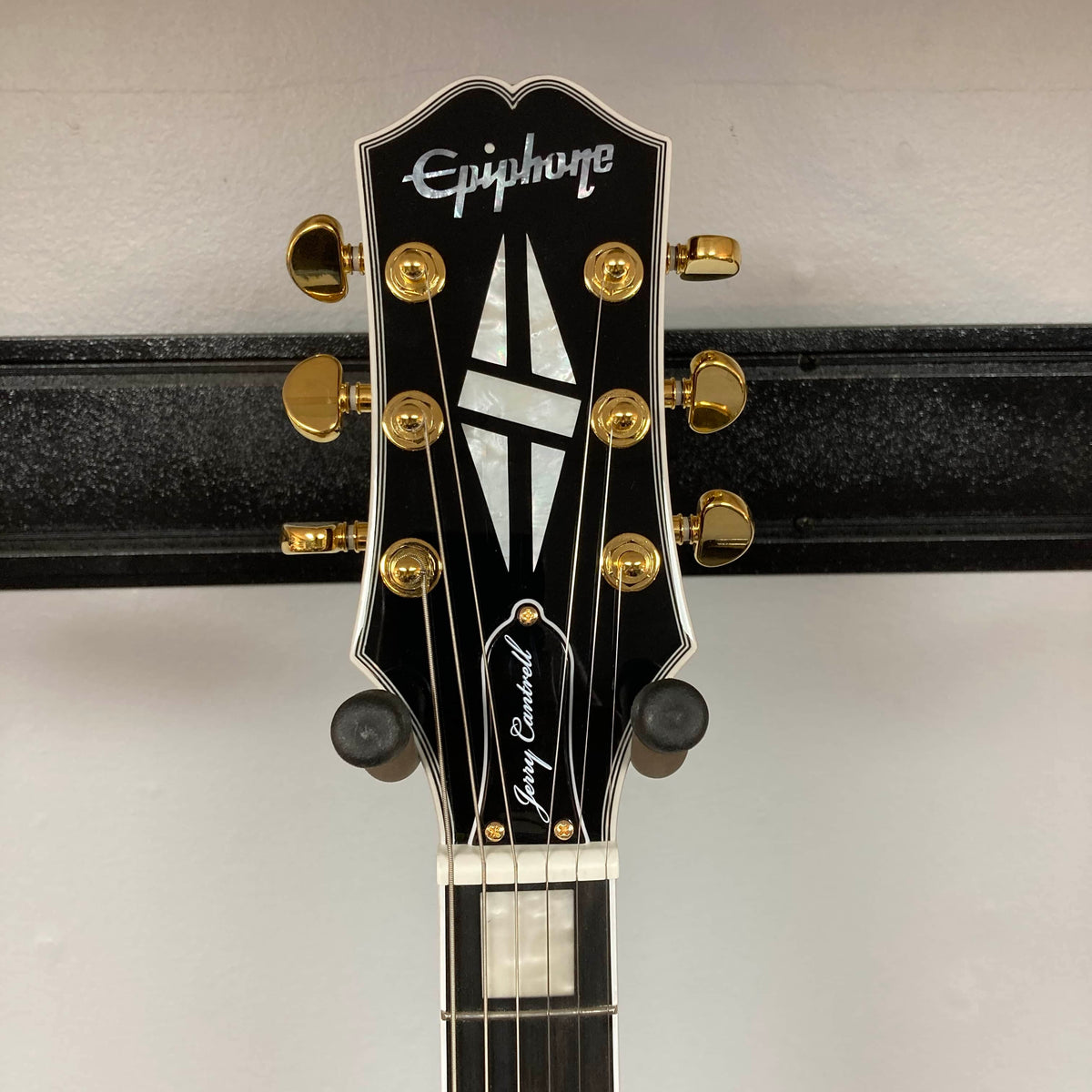 Epiphone Jerry Cantrell Wino Les Paul Custom in Wine Red with gold tuners and a black finish, featuring a stylish headstock, echoes the striking appeal of Gary Clark Jr.'s models—perfectly displayed on a wall hanger.
