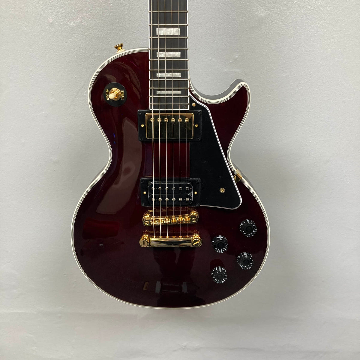 The Epiphone Jerry Cantrell Wino Les Paul Custom in Wine Red features gold hardware, a black pickguard, and four control knobs, shown on a plain white background; includes a custom hardshell case.