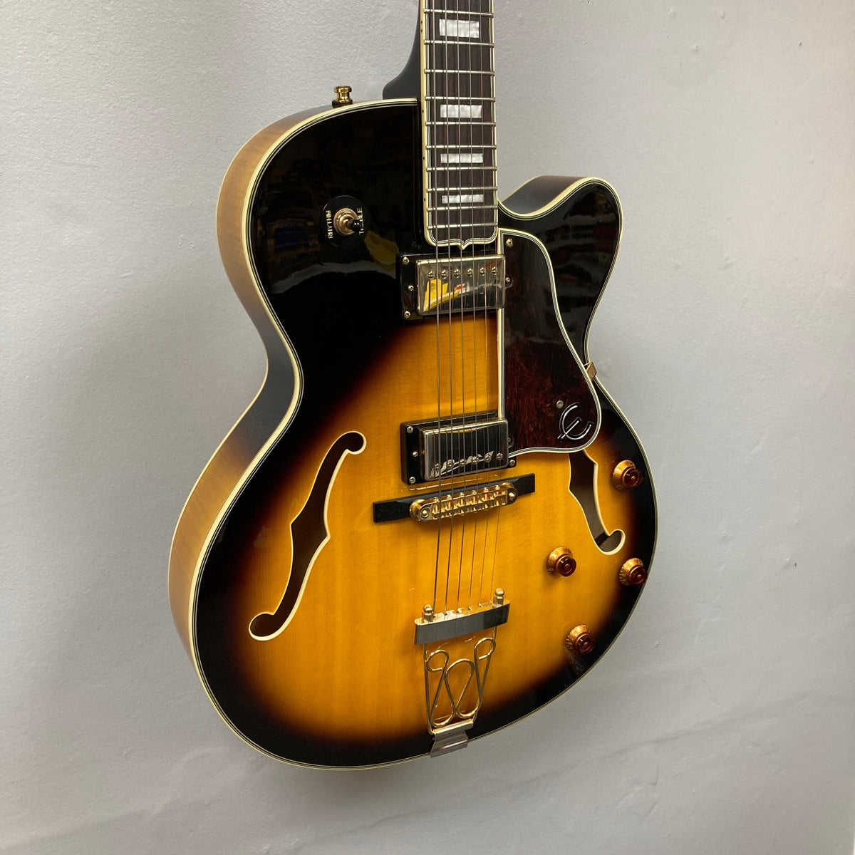 Epiphone Joe Pass Emperor II Vintage Sunburst guitar displayed on wall, highlighting its classic design and intricate details, used condition with case.