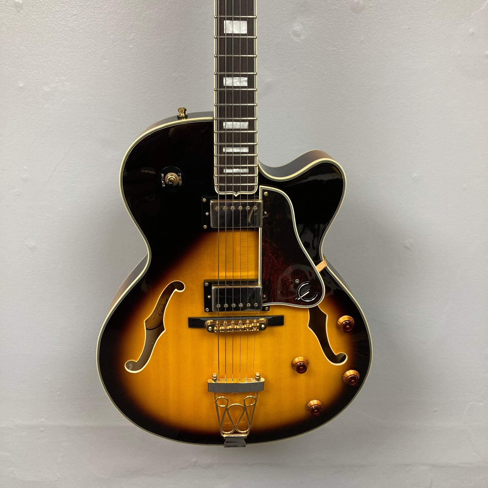 Epiphone Joe Pass Emperor II Vintage Sunburst guitar displayed on a wall, showcasing intricate strings and craftsmanship, used and includes a case.