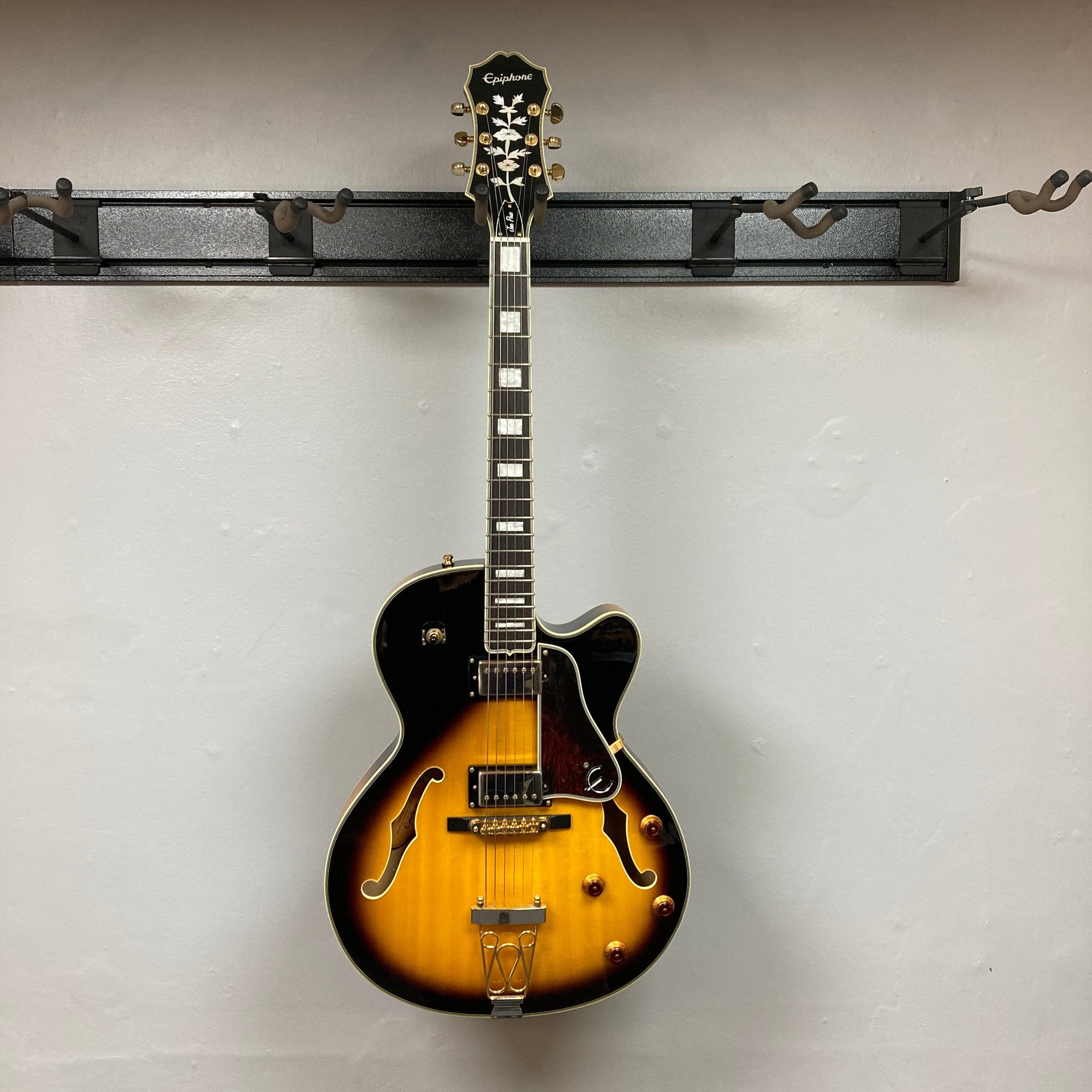 Epiphone Joe Pass Emperor II Vintage Sunburst guitar displayed on a wall, showcasing intricate strings and craftsmanship, used and includes a case.