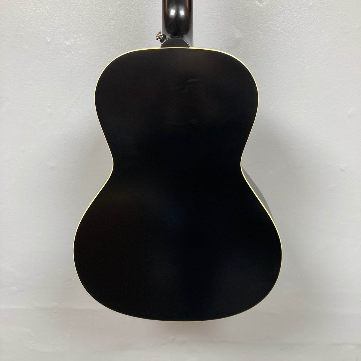 Back view of the Epiphone L-00 Standard Vintage Sunburst w/Gigbag, a small-bodied acoustic guitar by Epiphone, with a light-colored outline, hanging against a plain white wall.